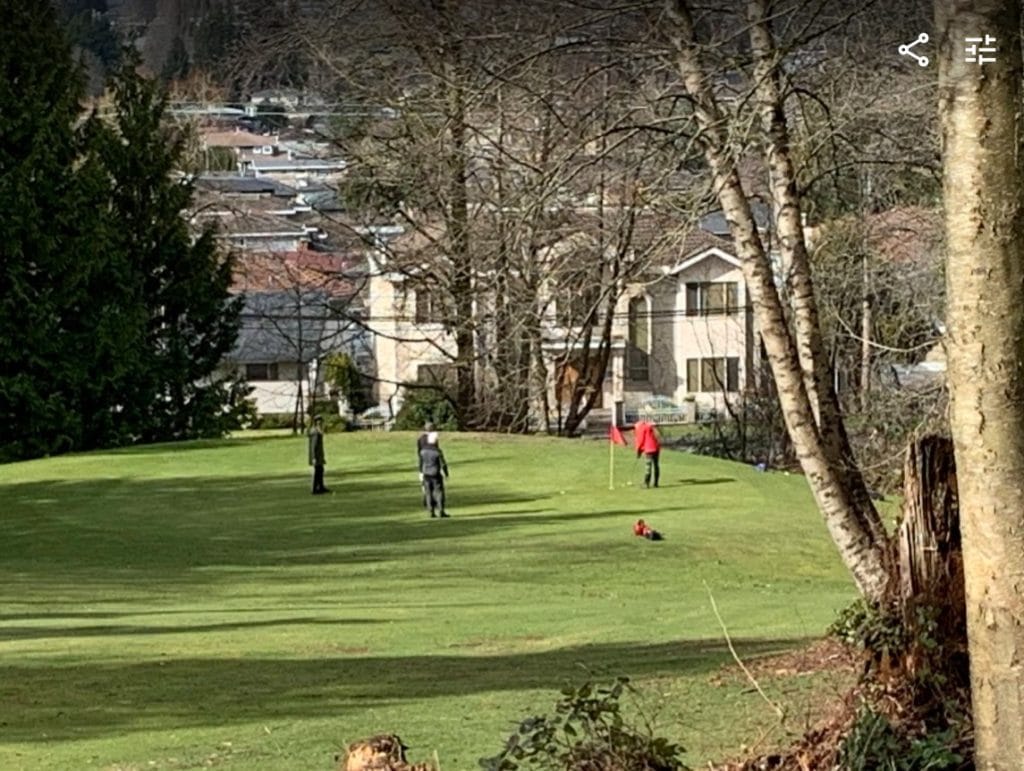 Group playing pitch and putt at Kensington Park in Burnaby, putting green with red flag and city view in background