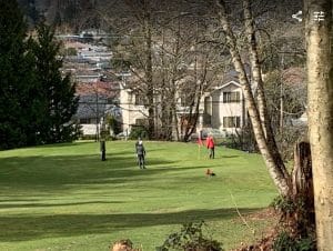 Group playing pitch and putt at Kensington Park in Burnaby, putting green with red flag and city view in background